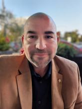 Eric, a bald white man with a beard wearing a brown sport coat with a royal blue collared shirt beneath.