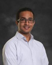 Image of a smiling middle aged Indian male wearing glasses and a white full hand shirt
